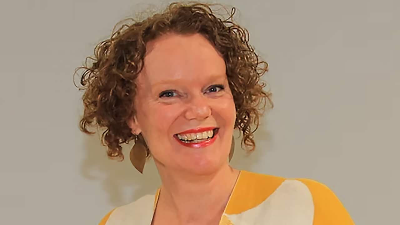 a middle aged woman with curly hair in a yellow and white patterned shirt smiling at the camera