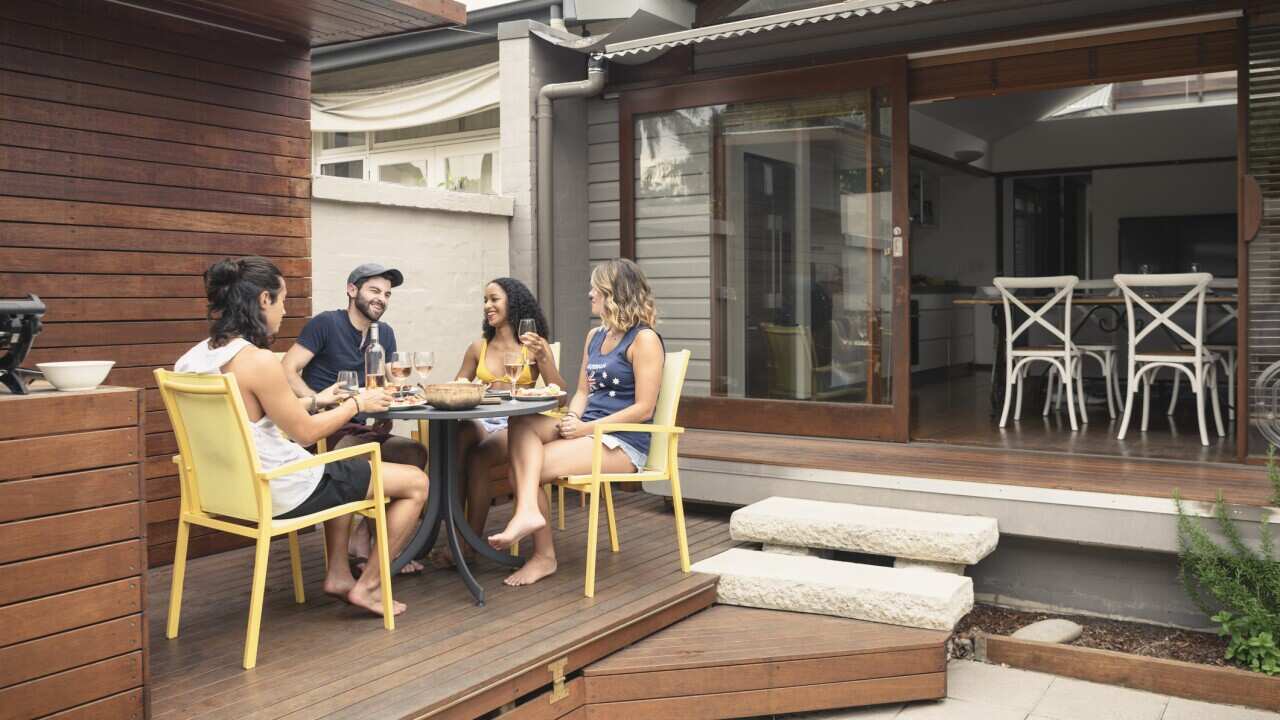 Group of four young adults relaxing on patio outside house with food and drink