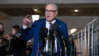 A man in a blue suit stands in front of microphones